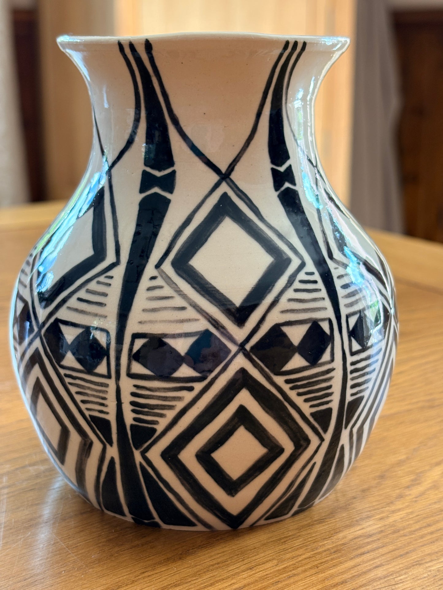 A black and white geometric diamond patterned ceramic vase sitting on a wooden table.